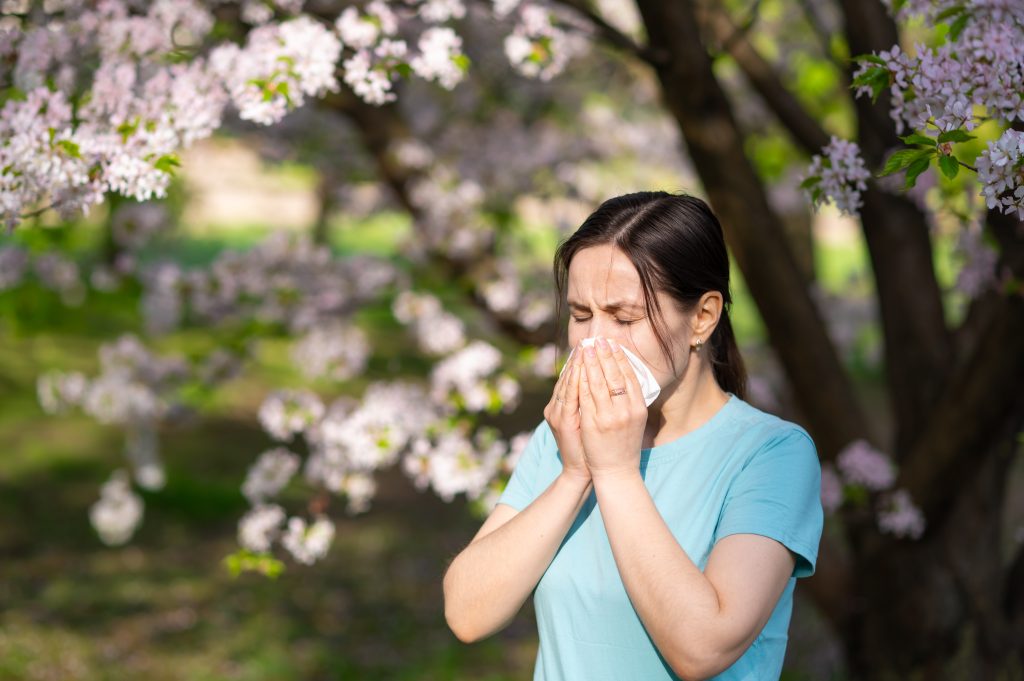 Frau vor blühendem Baum schnäuzt sich die Nase